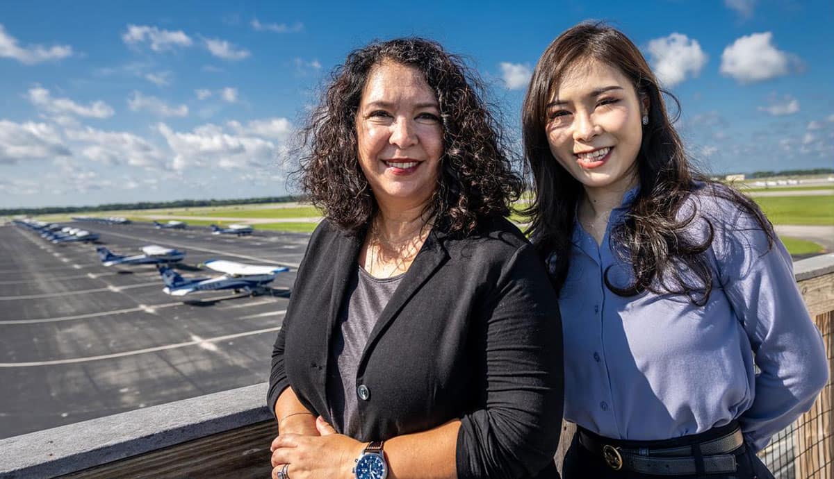 Two women stand in front of aircraft lot.