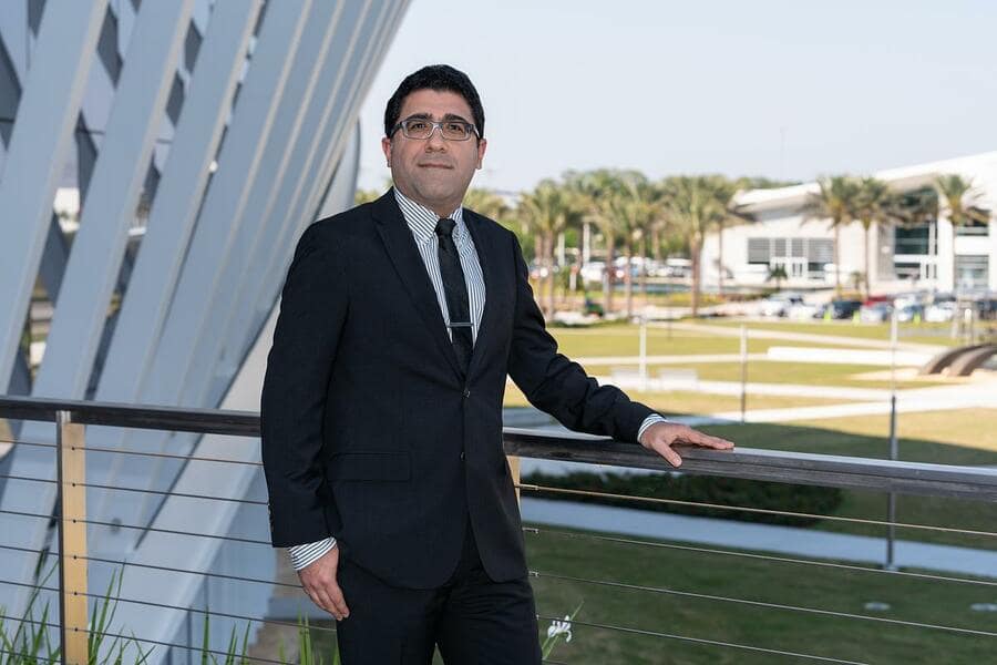 Man in suit poses for picture on college campus.