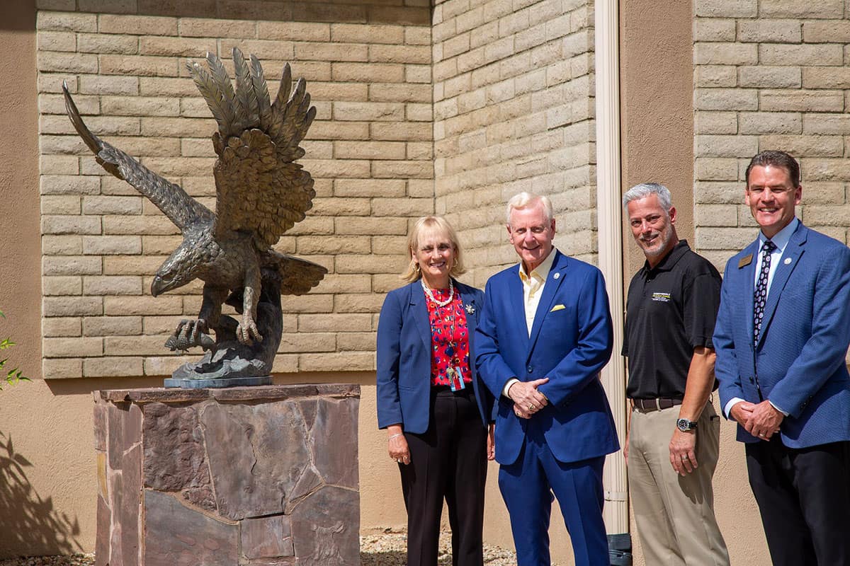 Four people stand next to eagle statue.