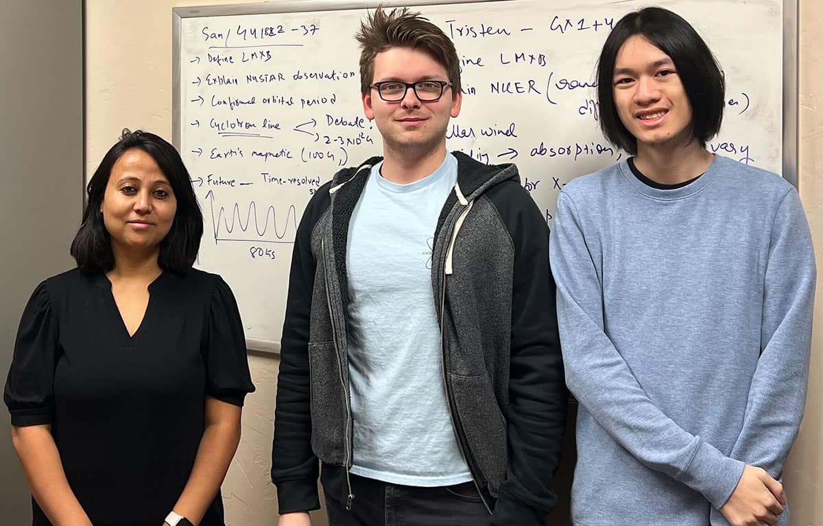 Three students stand in front of whiteboard.