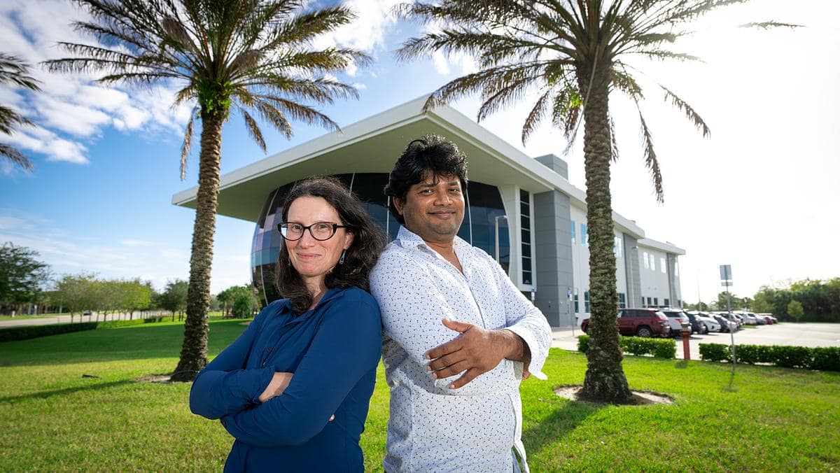Embry-Riddle professors stand back to back in front of a building framed by palm trees.