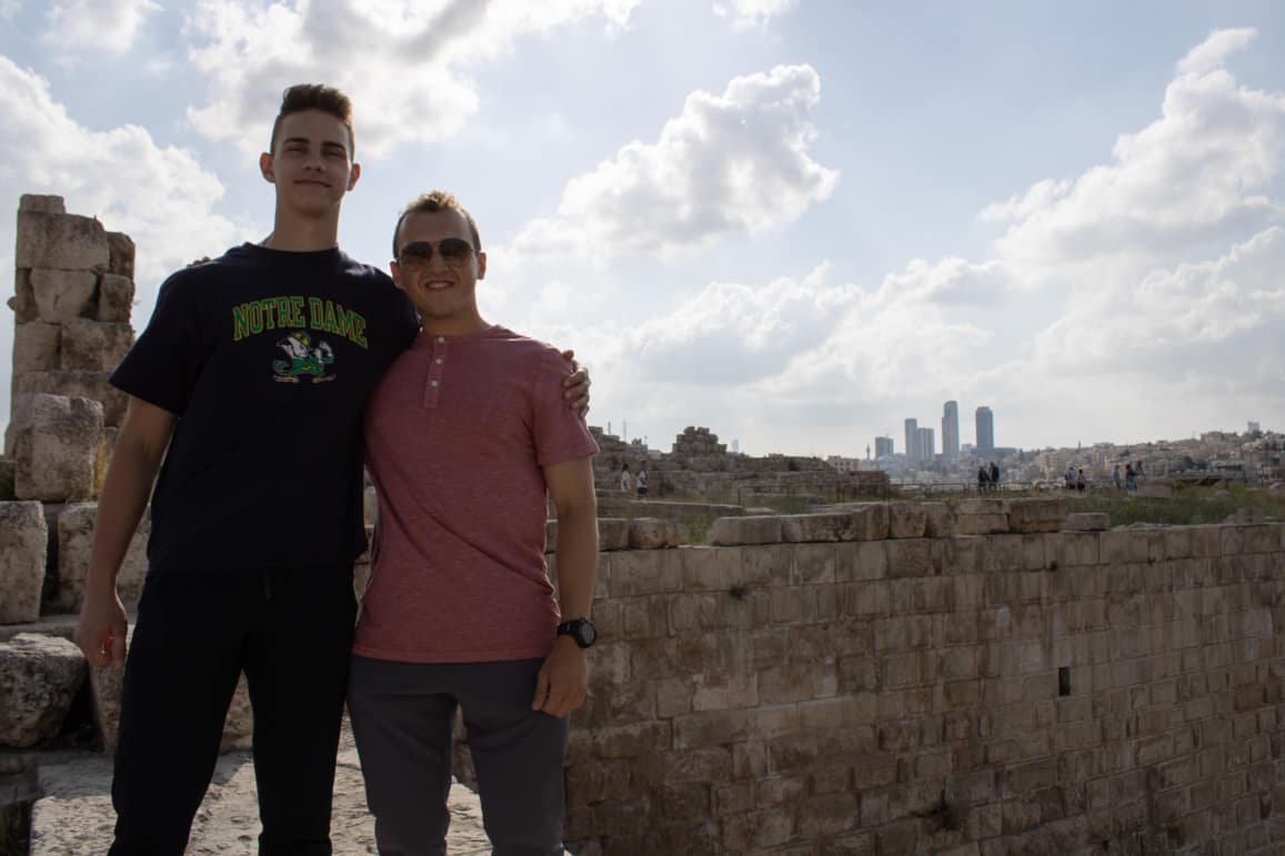 Two men pose with a city in the background.