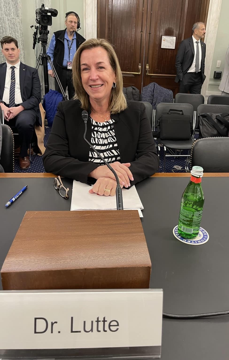 Woman sits at desk in congressional meeting.