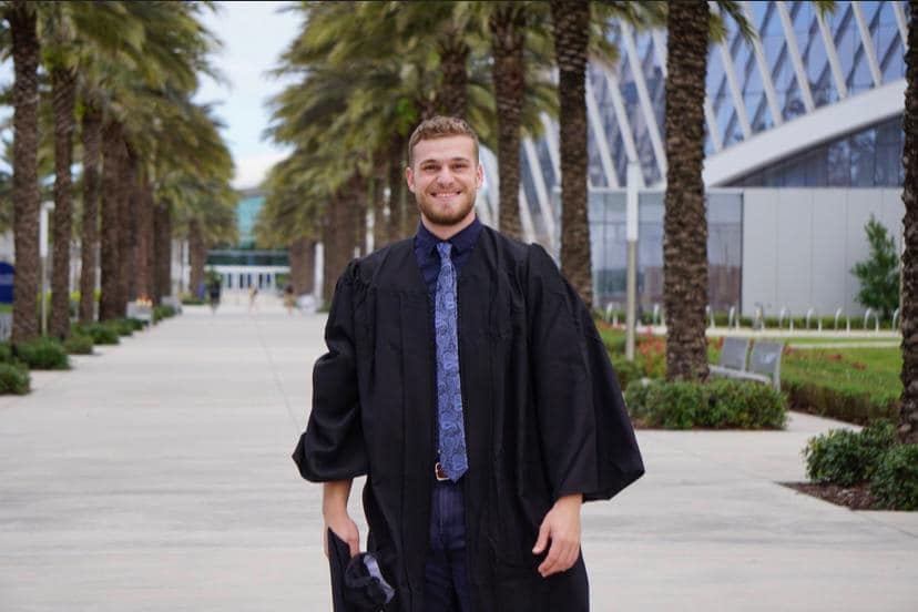 Man stands in cap and gown after graduation.