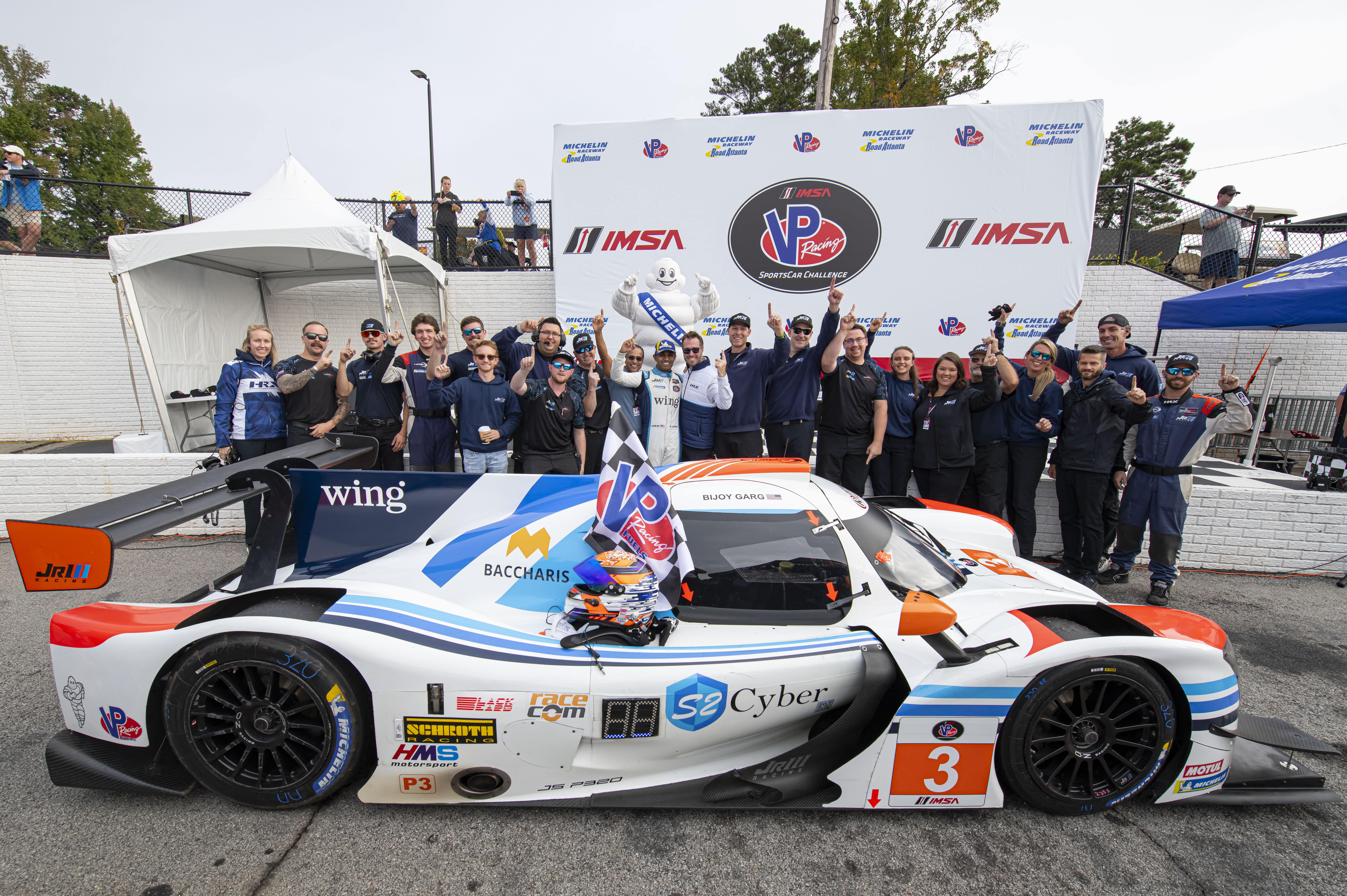 The Jr III Racing team holds up number one signs behind their car after winning a competition