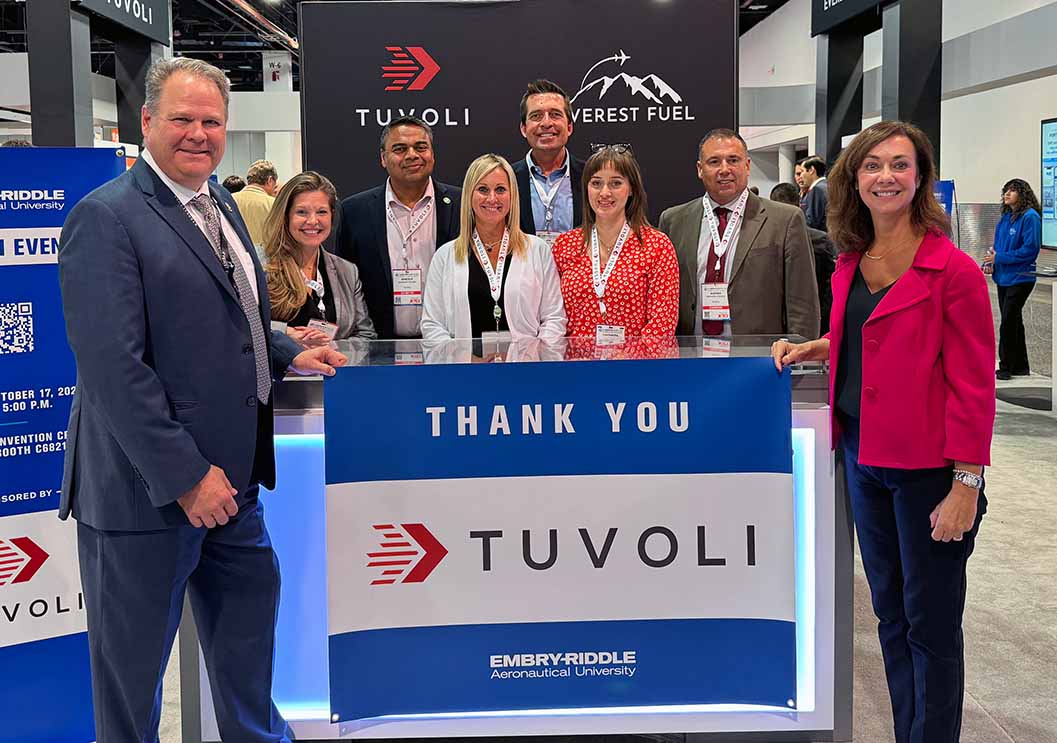 Eight people stand around a "Thank You, Tuvoli" sign at a convention.