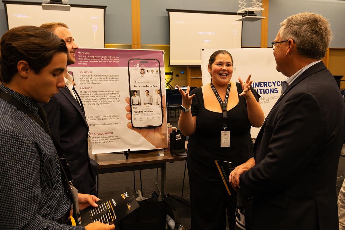 Women speaks to three men at convention booth.
