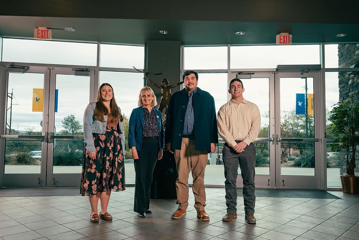 Two women (left) and two men (right) pose in the lobby area of a campus building.