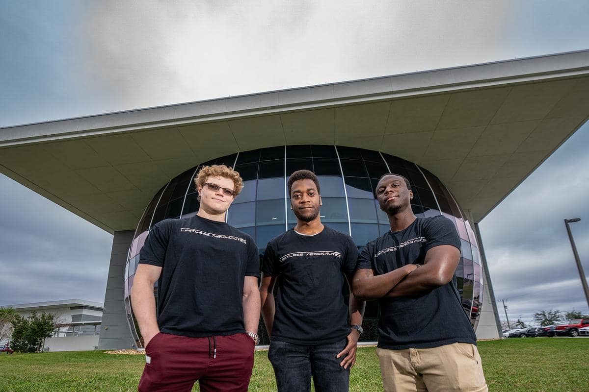 Three college students stand in front of building.