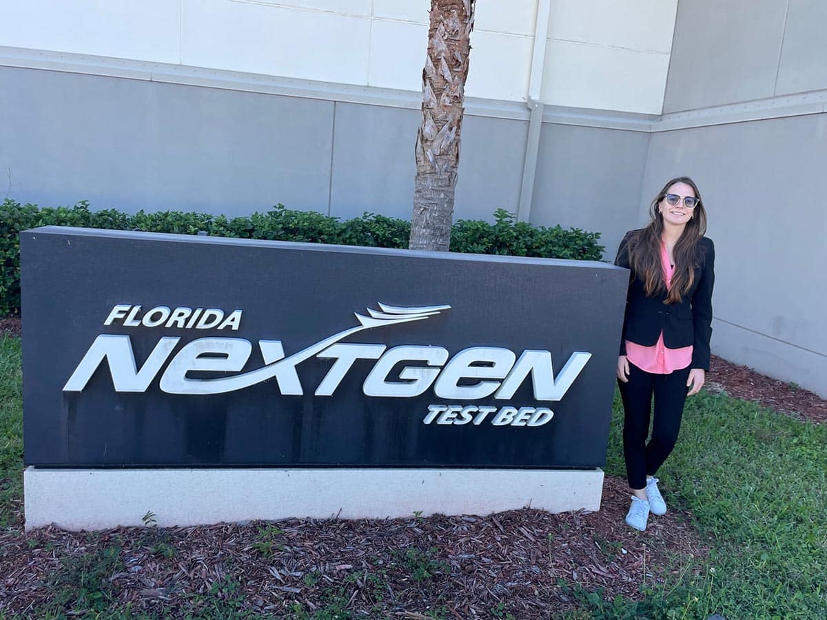 A young female student stands next to the Florida NextGen Test Bed sign outdoors