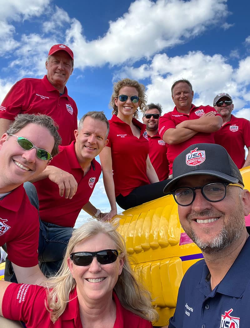 Group of people pose in red shirts in front of blue sky.