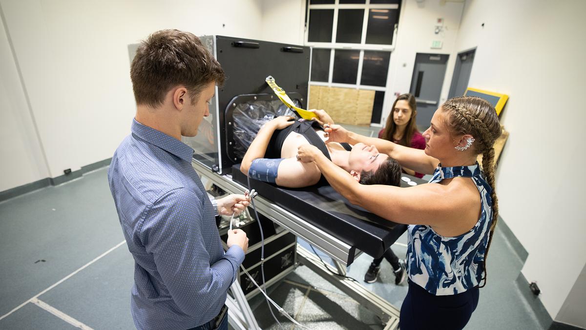 Student research assistant Isaac Kay (left) prepares for an experiment to simulate microgravity at Embry‑Riddle, as test subject James Palmer, has his harness tightened by Dr. Christine Walck, and student data analyst Megan Parker stands by. (Photo: Embry‑Riddle/David Massey)