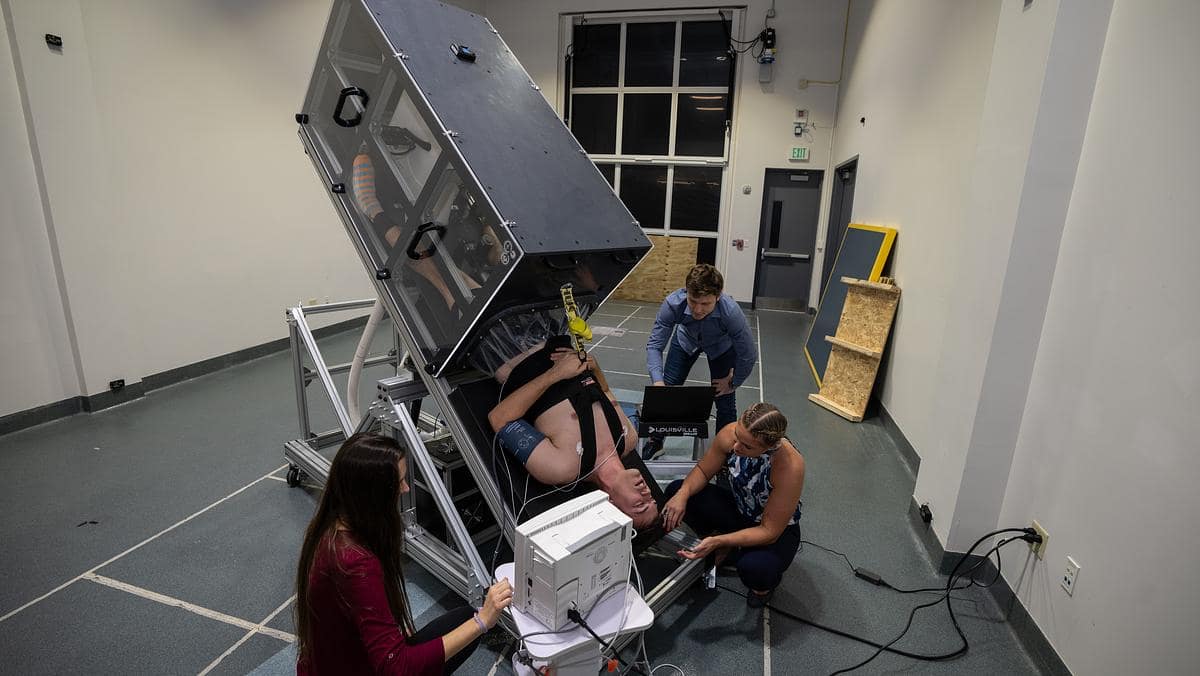 Student data analyst Megan Parker (left) monitors the pulse rate of test subject James Palmer, as he is tilted upside down. Dr. Christine Walck, along with student research assistant Isaac Kay, work with the device that simulates microgravity while analyzing intraocular pressure. (Photo: Embry‑Riddle/David Massey)