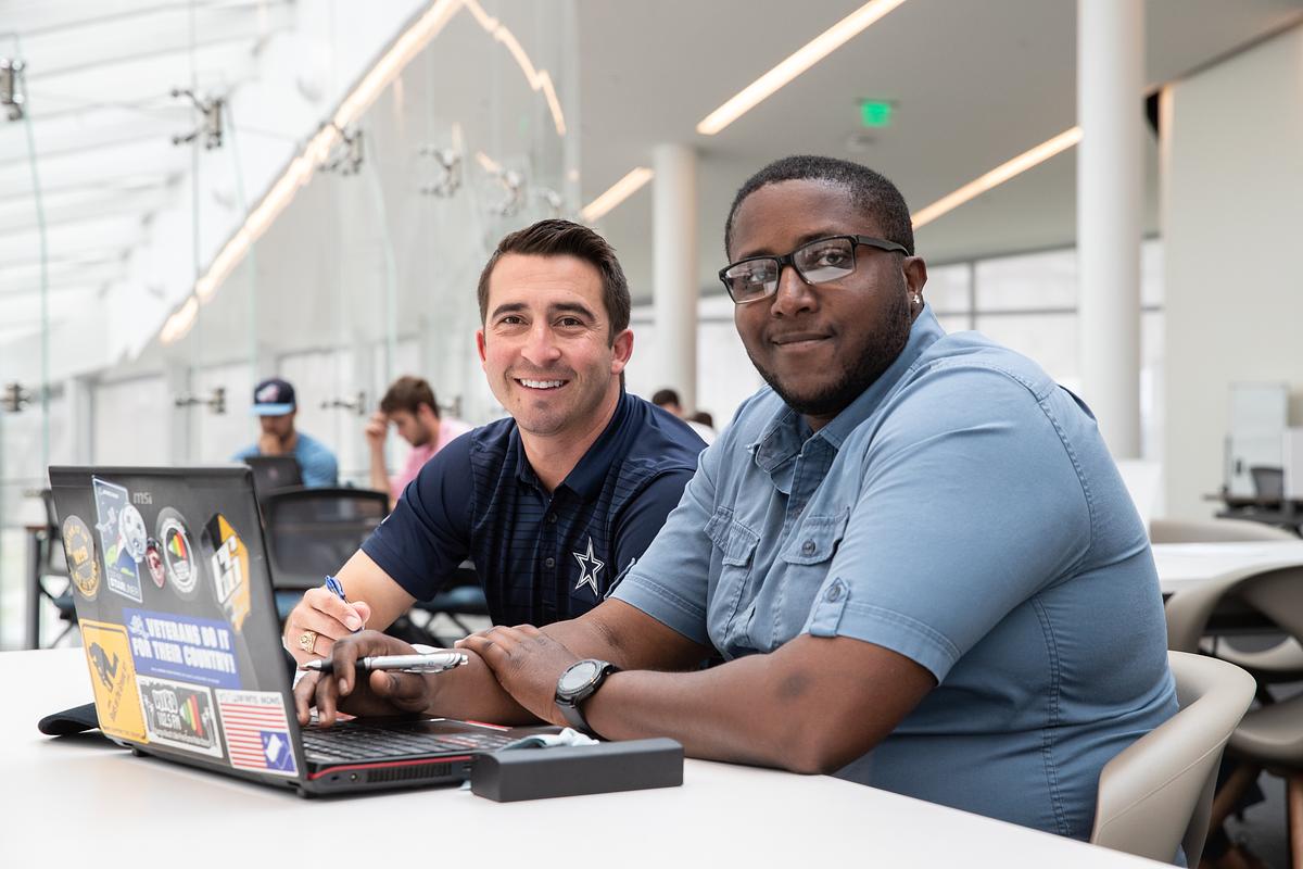 Two Embry-Riddle students sit together working on a laptop, smiling at the camera