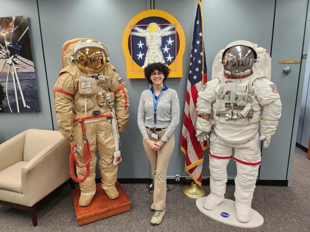 Aerospace Engineering senior Liz Bosch stands beside two spacesuits — one from Roscosmos (left), called Орлан (Orlan in English pronunciation), the other a NASA Extravehicular Activity suit.