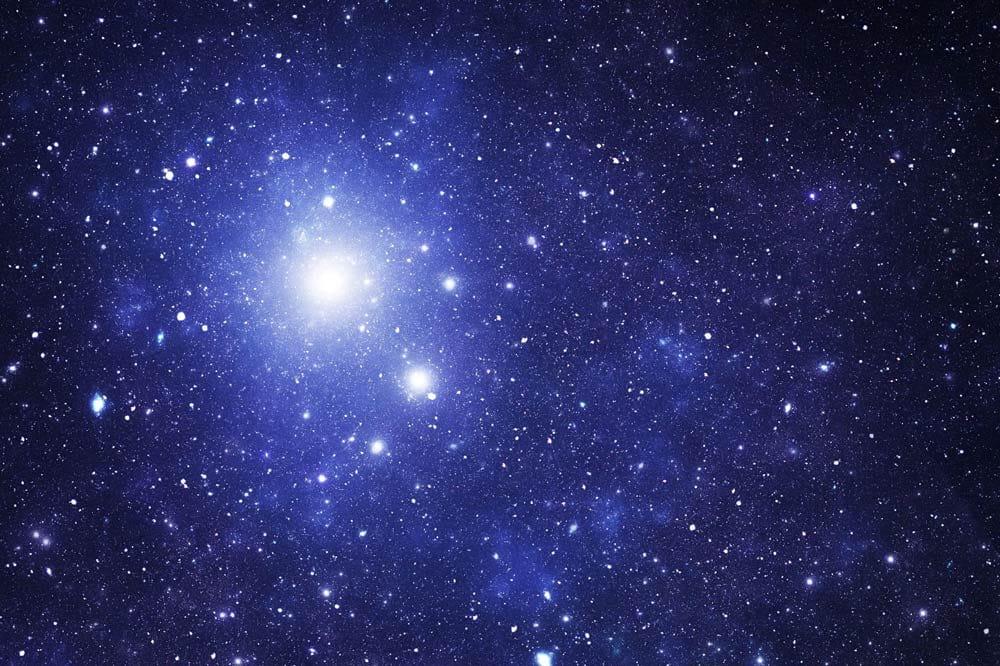 Dense star field with bright central cluster and surrounding galaxies in deep space view.
