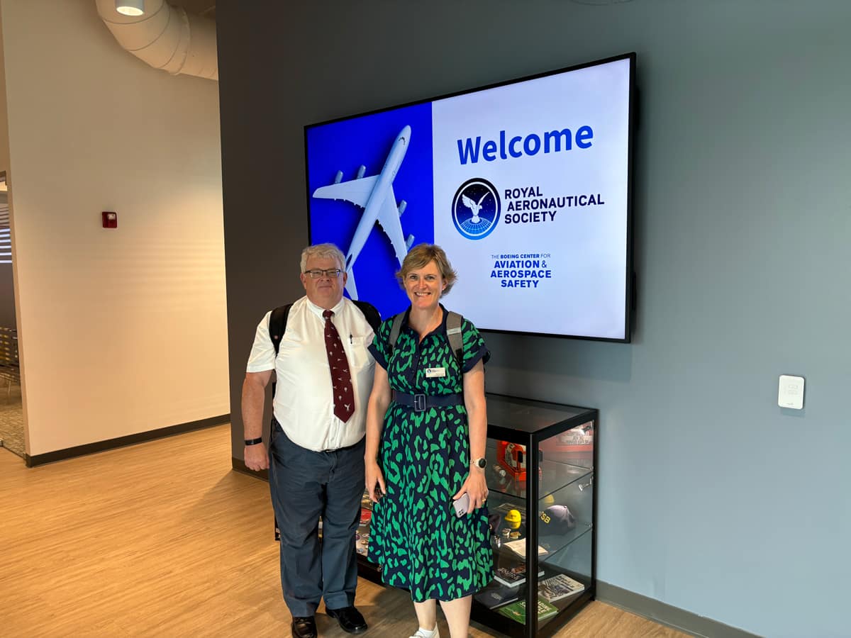 Visitors standing beside display screen reading 'Welcome Royal Aeronautical Society' at aviation and aerospace safety center.