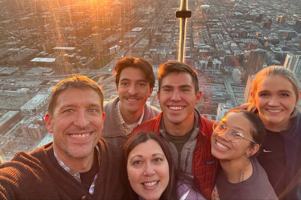 A group taking a selfie at an observation deck with a city skyline below at sunset.