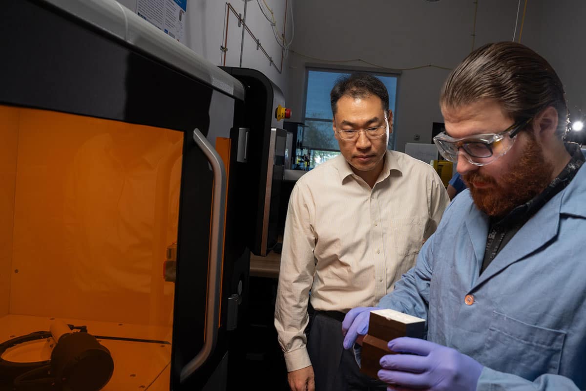Dr. Daewon Kim, professor of Aerospace Engineering, works with Embry‑Riddle Ph.D. student Nicholas Reed at the Lithoz CeraFab Multi 2M30. Reed is holding the “build plate,” which he has removed from the printer to inspect parts during their fabrication. (Photo: Bill Frenette-Huffman/Embry‑Riddle)