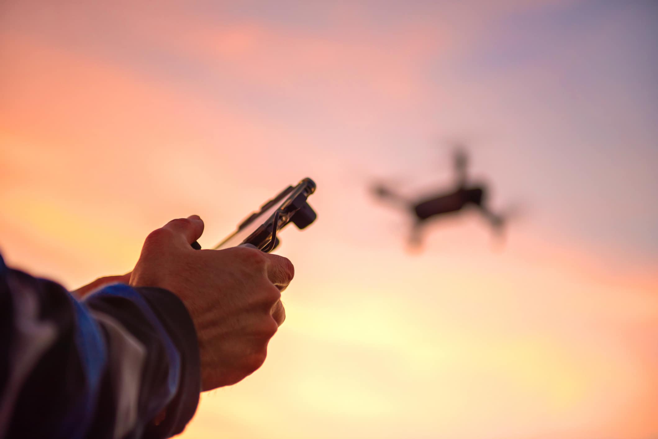 A drone flies in the sky at sunset; the hands holding the controller are in the foreground.