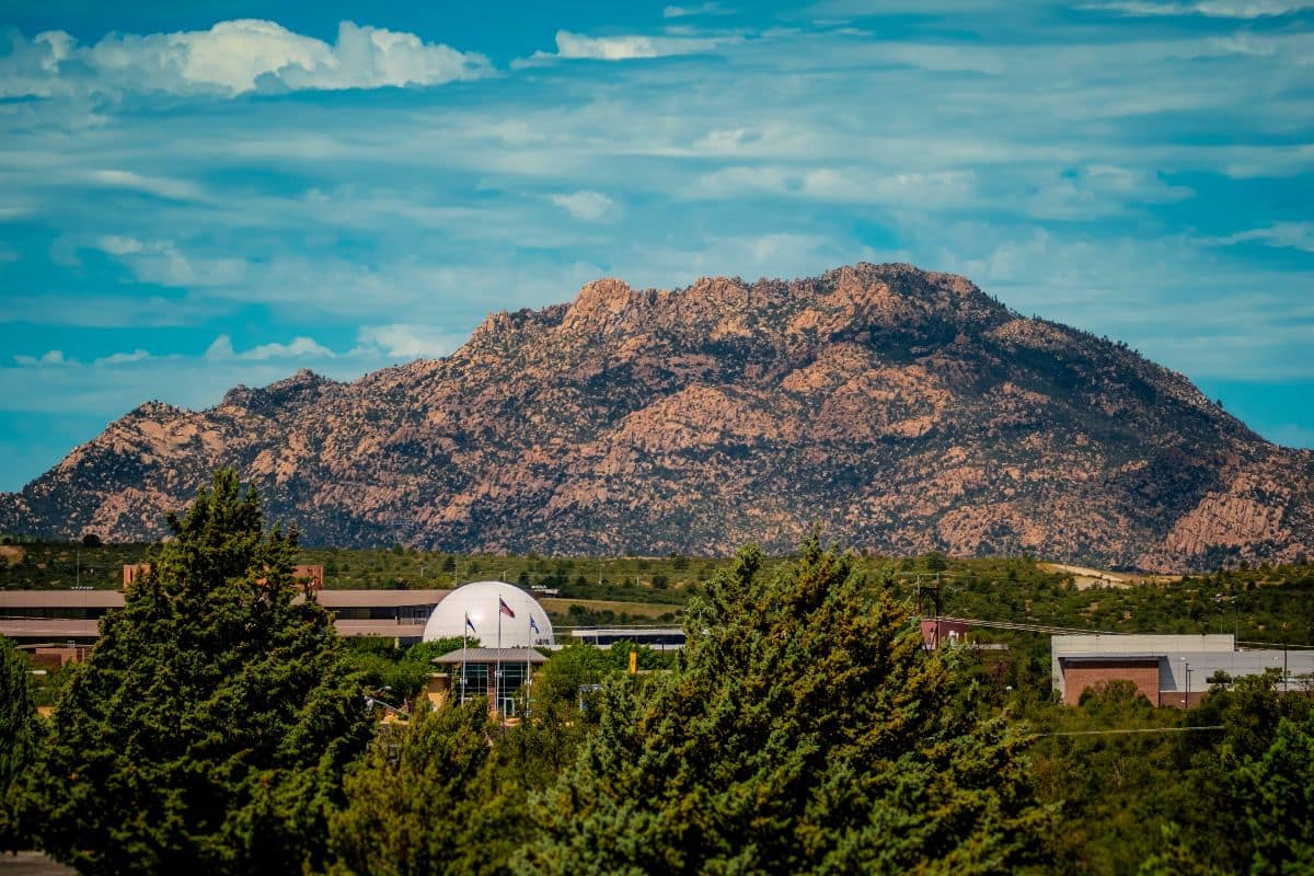 Granite Mountain rising behind Embry-Riddle Prescott campus with observatory dome and surrounding academic buildings under a partly cloudy sky.