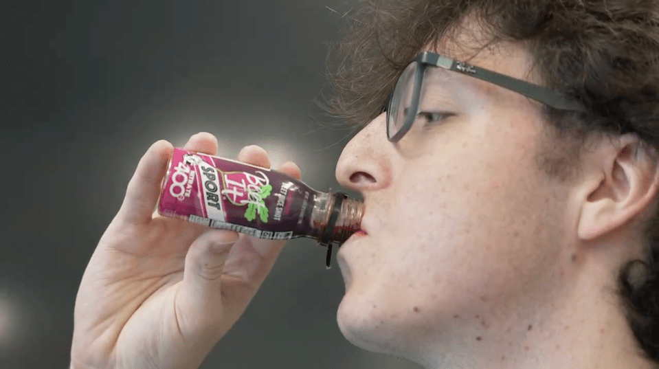 Man drinks beet juice from small bottle.