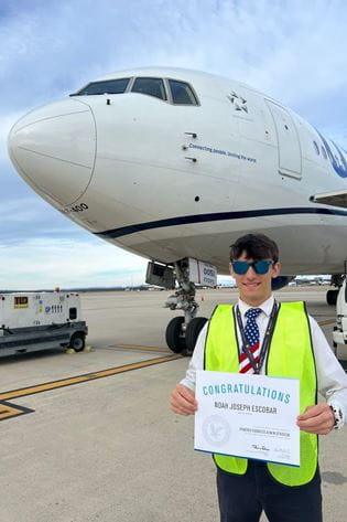 Escobar stands on the ramp in front of a United 767 while holding his acceptance letter to Embry-Riddle Aeronautical University's Prescott Campus, where he is studying Aviation Business Administration.