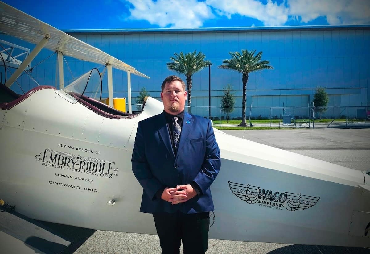 Jacob Pritchard stands in front of a vintage Embry-Riddle plane. 