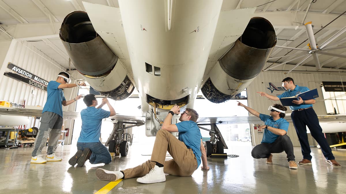 Five students examine aircraft. Two students are wearing virtual reality headsets.