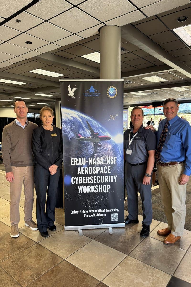 Four people stand next to a banner displaying an airplane flying above the Earth.
