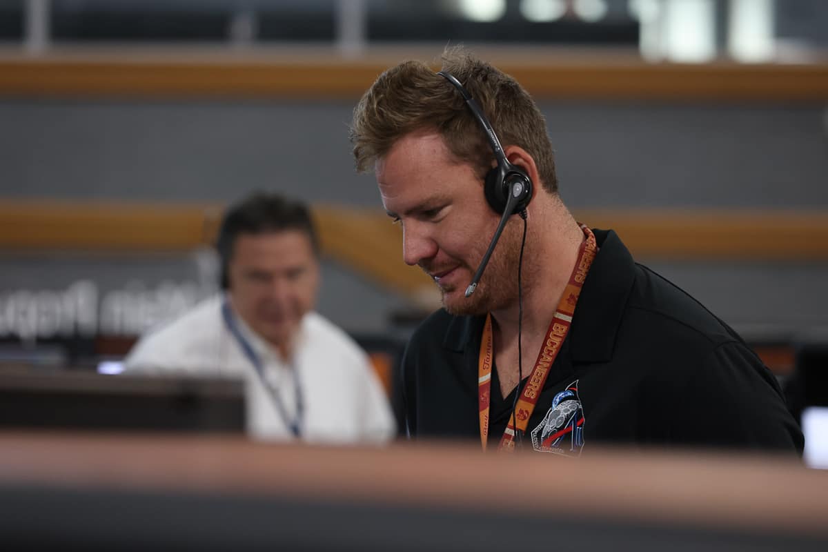 Man with headset stands in launch control center looking at computer screen.