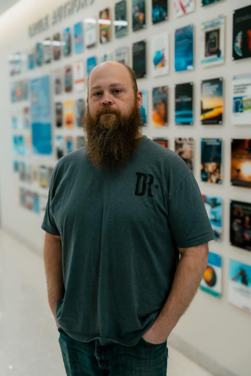 Andrew Lamer stands in front of artwork on a wall.