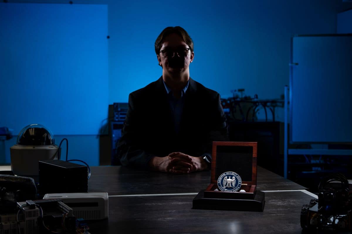 Man sits at desk in darkness with NSA award on desk.