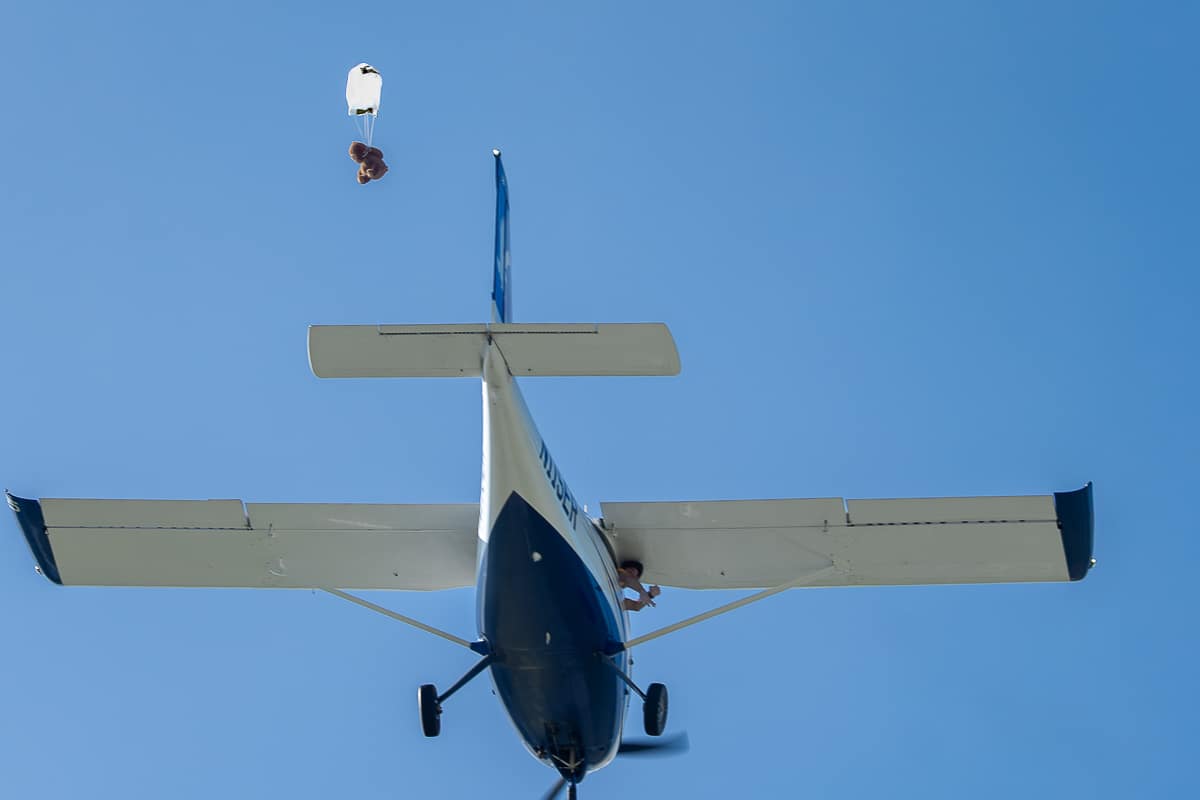 Airplane against blue sky with teddy bear descending from a small parachute.