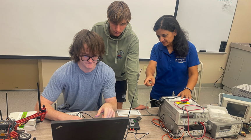 Three people in front of a computer and other tech equipment