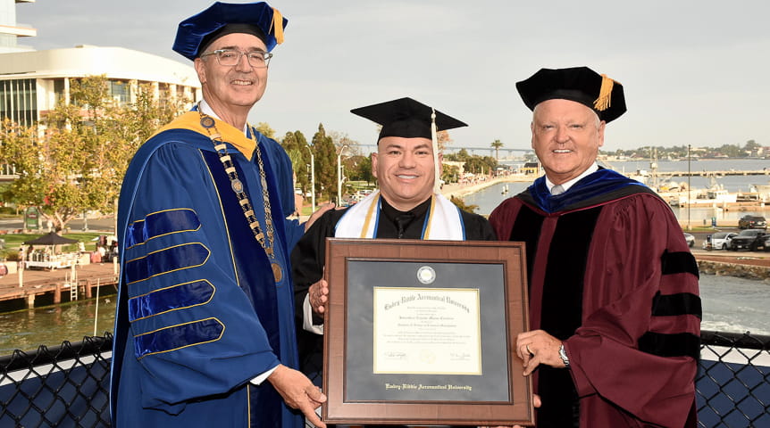 President Butler and Chancellor Watret stand next to 100,000th graduate holding diploma