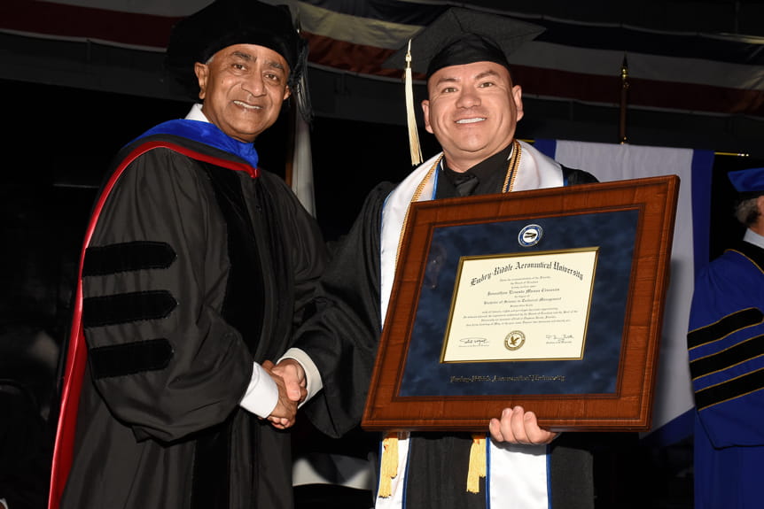 Man holds up diploma while shaking dean's hand at commencement