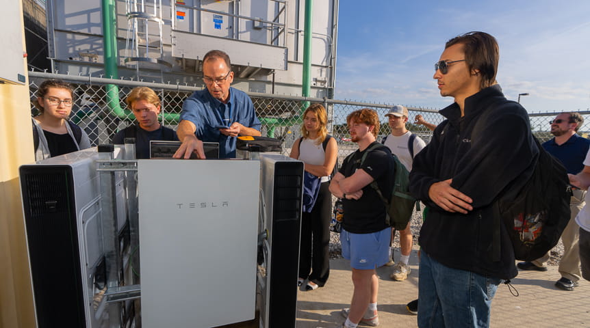 A half-dozen people around a Tesla Powerwall battery system