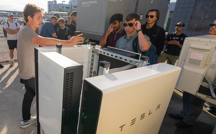 A Tesla Powerwall surrounded by a half-circle of people