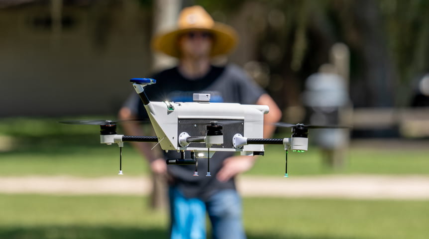 Person operating a white drone in an open grassy field during daytime