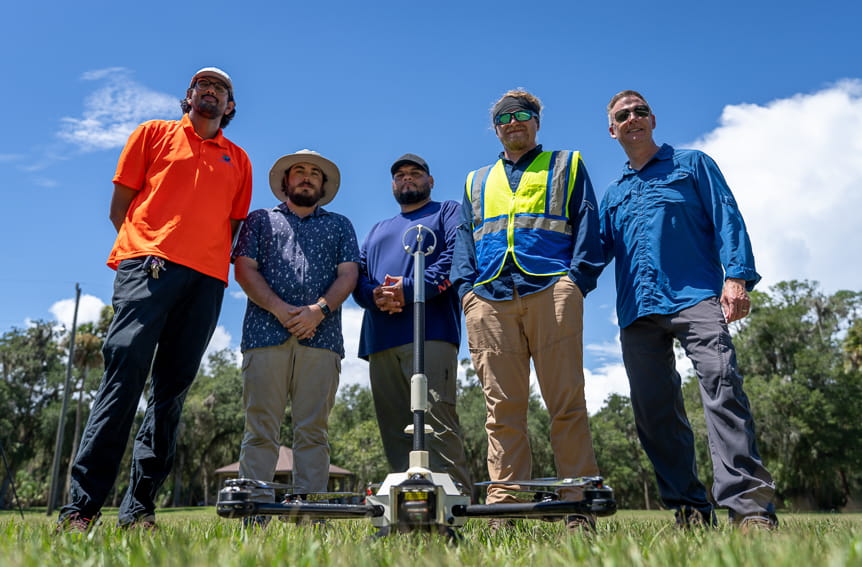 Five professionals standing with a meteorologically instrumented multirotor in a sunny grassy field