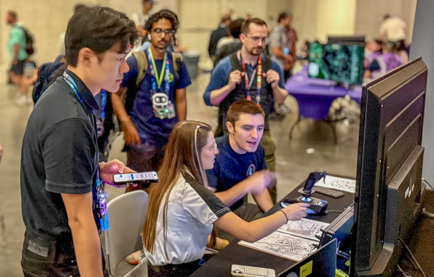 Three people in front of a computer screen where participants are undertaking the CARD GPS spoofing challenge at DEF CON