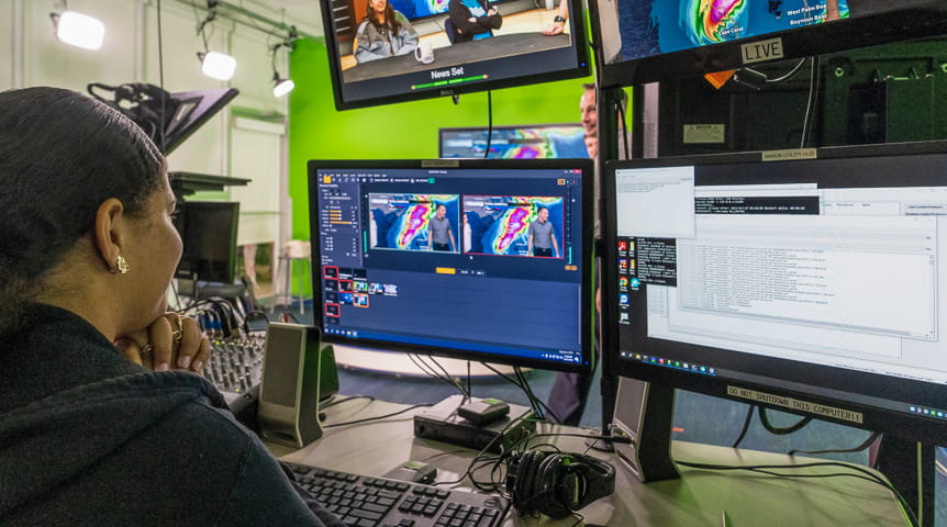 Woman in front of four computer screens showing hurricane path in a green screen room used for meteorology at Embry-Riddle. 