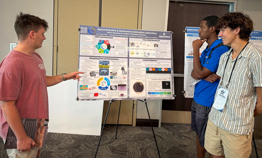 Three students stand in front of a poster on robotics research