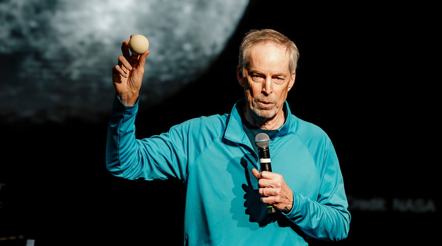 Astronaut Jim Wetherbee holds a ball in front of an image of the moon