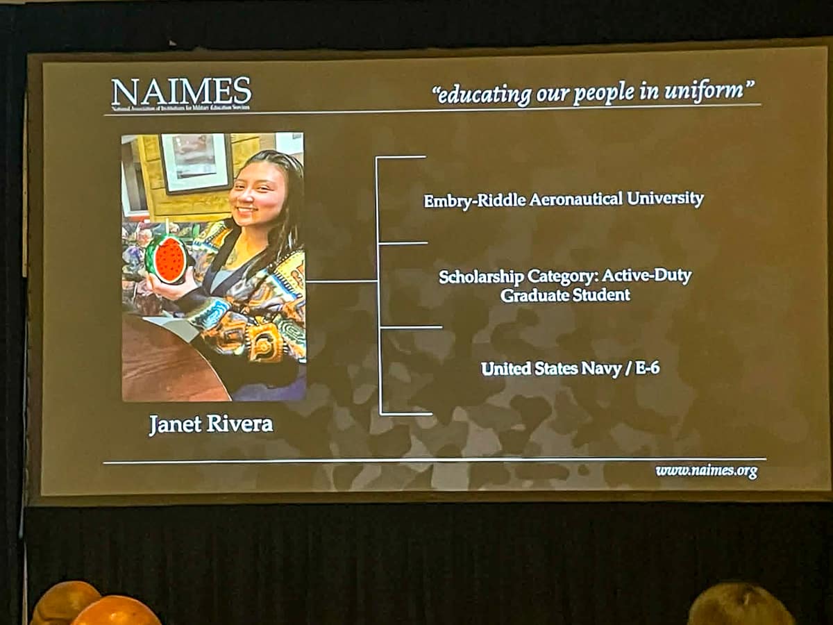 Large projector screen with image of woman in corner and rows of text