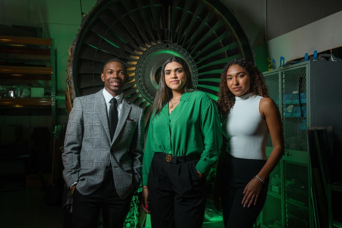 Daytona Beach Campus students Benjamin Carter, Jesika Geliga-Torres and Nichole Fajardo pose in business wear in front of a jet engine fan.
