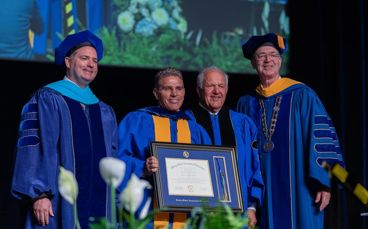 Four men in cap and gowns, including one holding a diploma