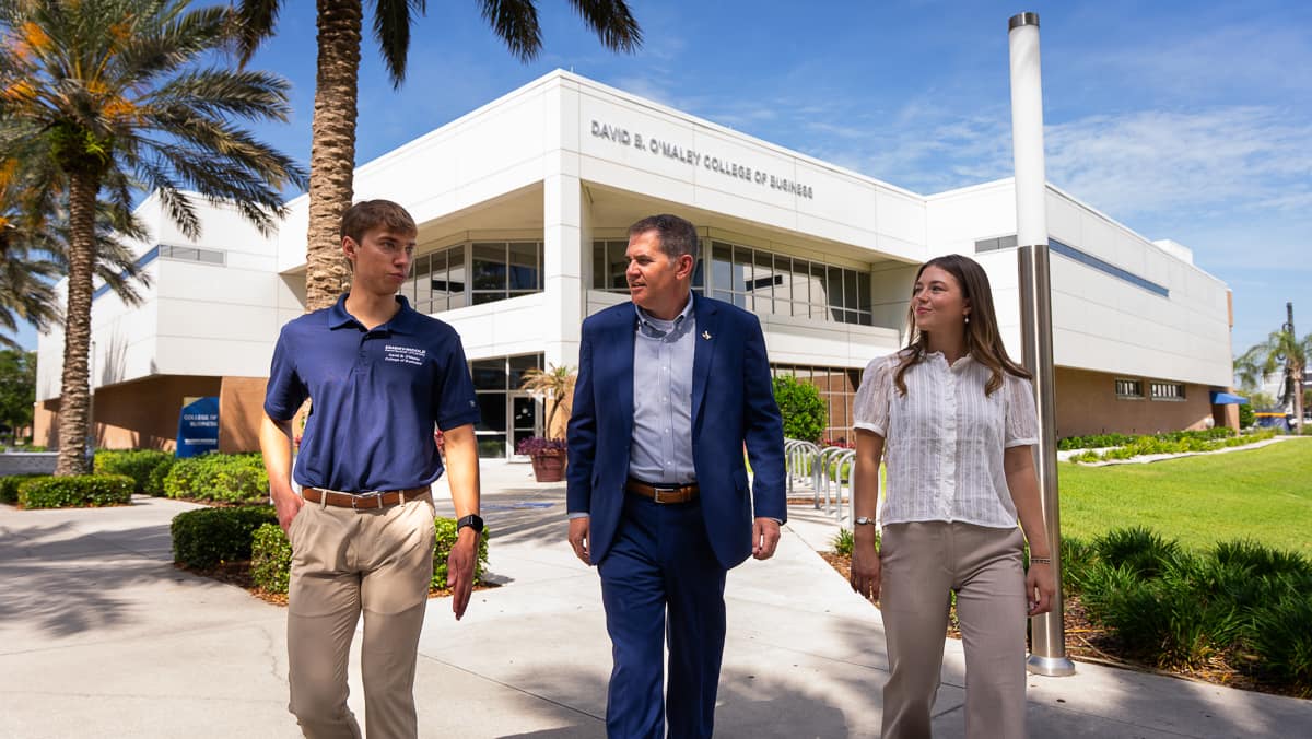 Two men and a woman on a path in front of a building
