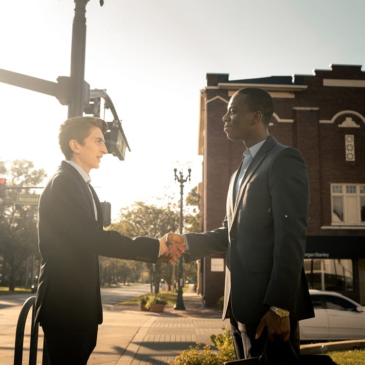 Embry-Riddle business students shake hands while standing on the sidewalk before meeting downtown